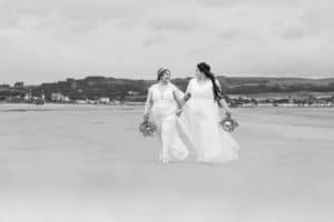 Two brides walking along Ayr beach holding hands